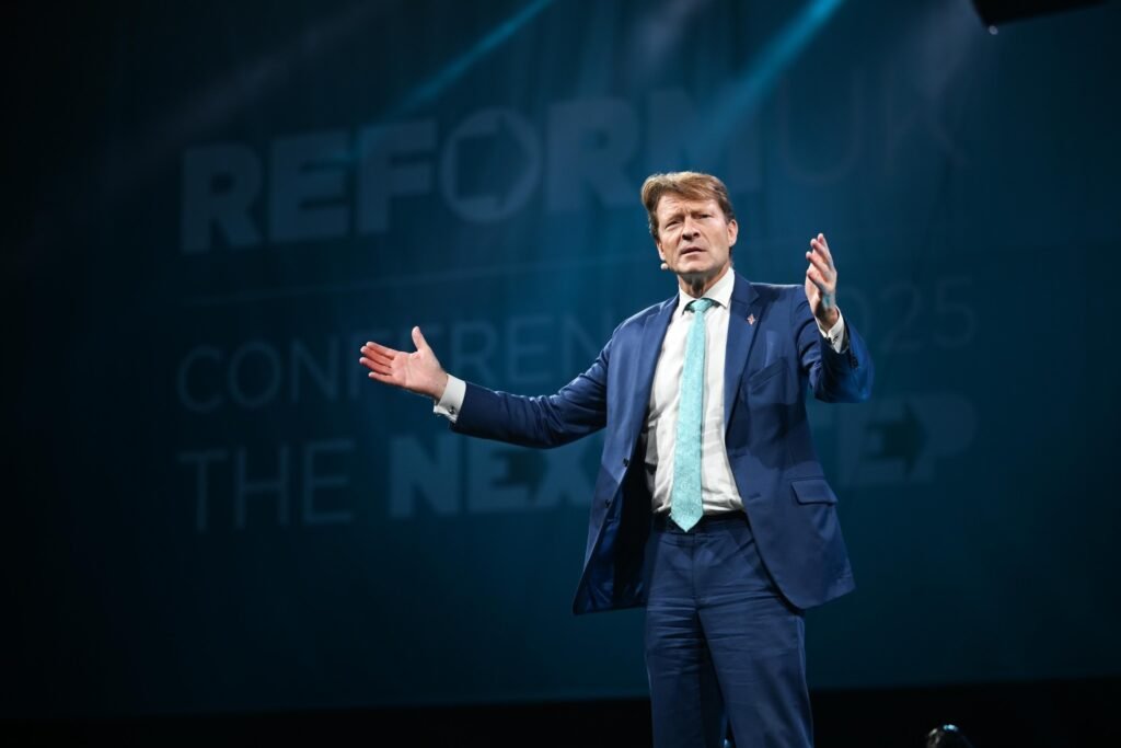 Richard Tice speaking at Reform UK Birmingham conference September 2025 wearing dark suit behind party podium with microphone
